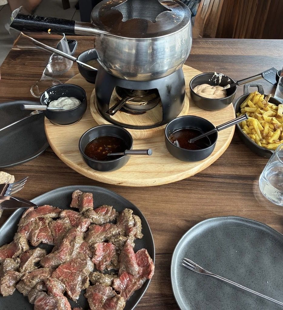 Fondue de ternera con la carne cruda, patatas fritas y salsas alrededor del caldo