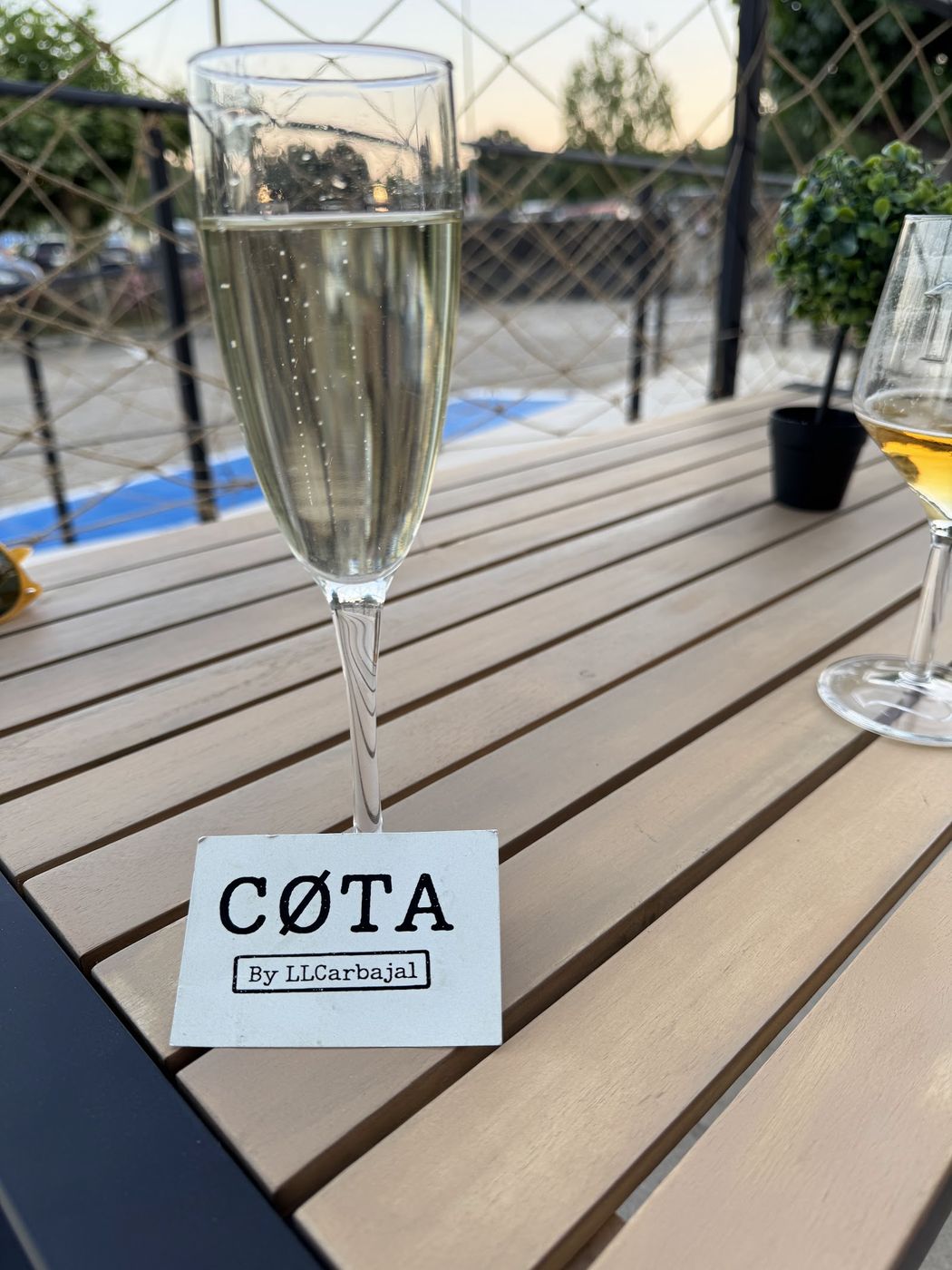 Copa de espumoso en una mesa de madera de la terraza, con la tarjeta de CØTA